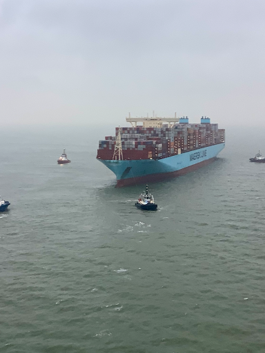 Großes Containerschiff auf dem Wasser, umgeben von mehreren kleinen Booten.