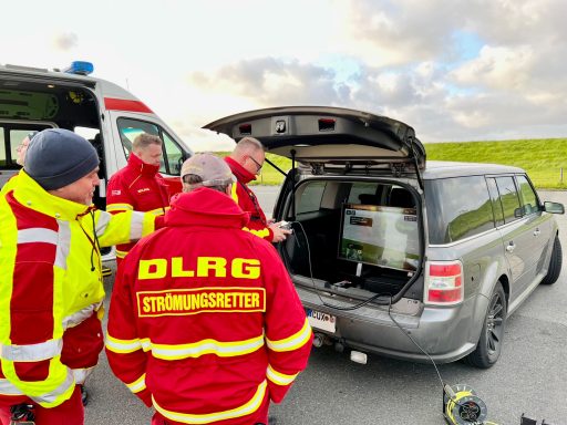 DLRG-Einsatzteam in roten Jacken, bespricht sich neben einem Fahrzeug und einem Krankenwagen.